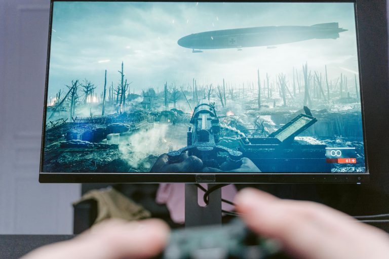 A person playing a video game on a high-resolution monitor, showcasing a war-themed landscape.